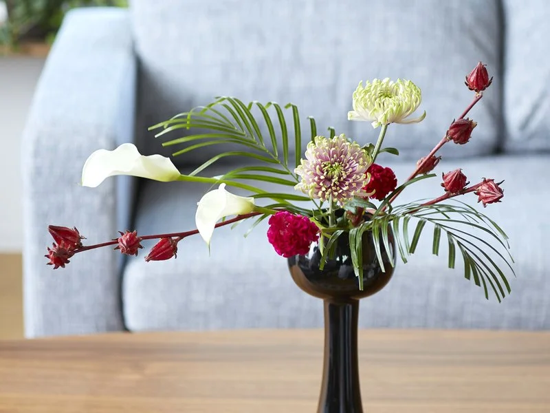 W. 花瓶・水盤月2回コースのお届け例（黒い花器に葉ものと赤い実を生けたもの）